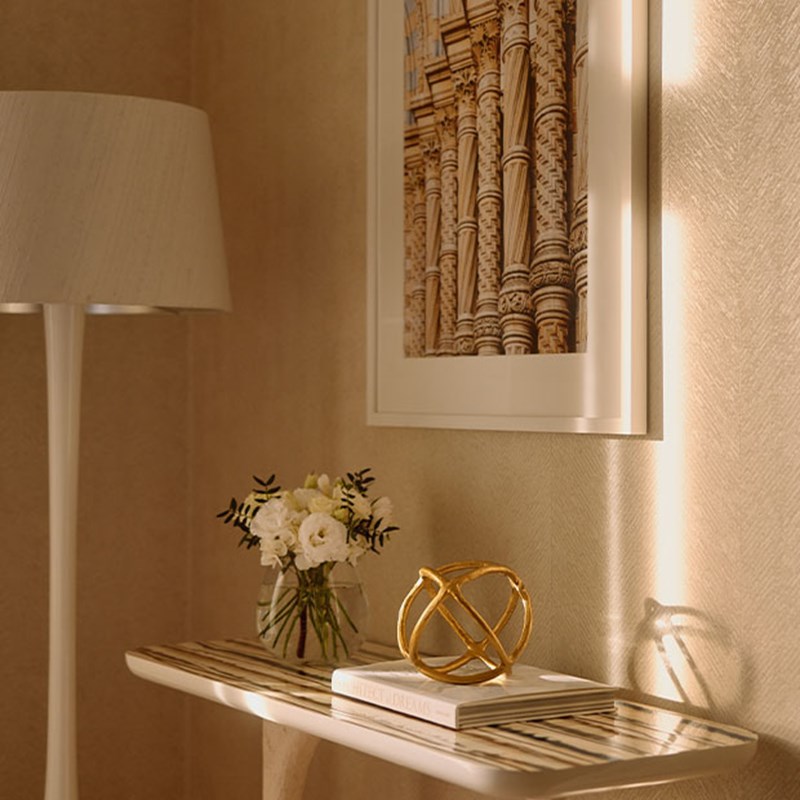 Decorative console table holding a gold geometric sculpture and stacked books, below a framed photograph of ornate columns and beside a floor lamp.