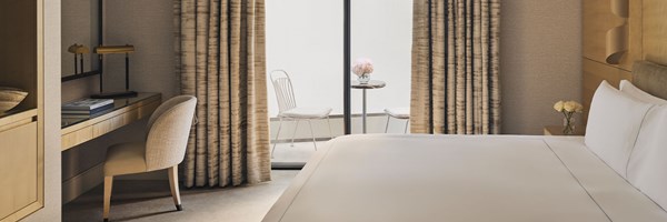 Calm hotel bedroom with a king-sized bed, writing desk, and access to a private courtyard balcony with two chairs and a table.