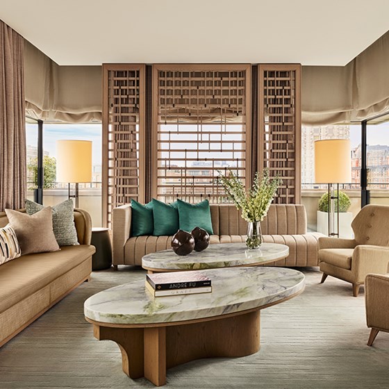 Spacious penthouse living room with floor-to-ceiling windows, neutral-toned seating, green accent pillows, and a marble coffee table with modern décor.