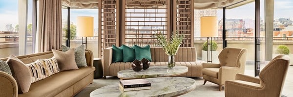 Spacious penthouse living room with floor-to-ceiling windows, neutral-toned seating, green accent pillows, and a marble coffee table with modern décor.