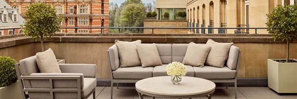 Private penthouse terrace with beige cushioned sofas, potted greenery, and views of historic city architecture and treetops.