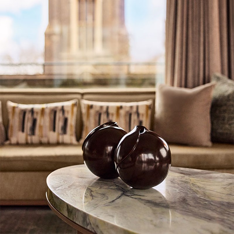 Detail view of a marble coffee table with two glossy dark ceramic vases, set against a backdrop of a neutral-toned sofa and patterned cushions.