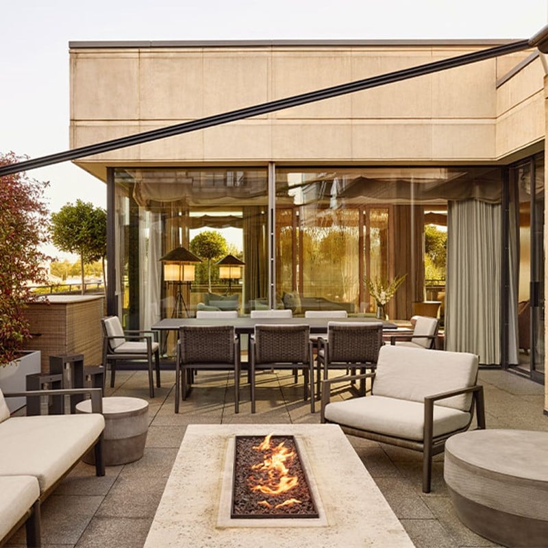 Spacious terrace with fire pit, dining table, and lounge seating outside a glass-walled suite.