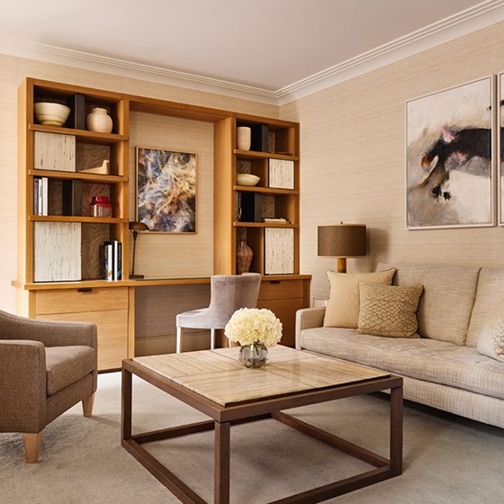 A comfortable lounge area with soft neutral-toned furnishings, a built-in writing desk framed by open bookshelves, and contemporary abstract artwork.
