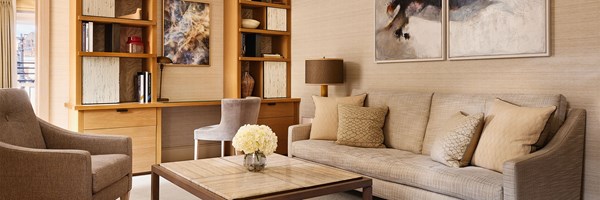 A comfortable lounge area with soft neutral-toned furnishings, a built-in writing desk framed by open bookshelves, and contemporary abstract artwork.