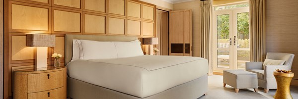 A serene bedroom featuring a tall wood-panelled headboard, a king-size bed dressed in crisp white linens, and French doors opening to a private garden terrace.