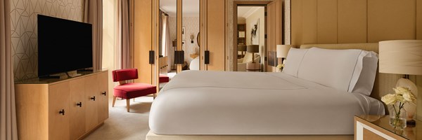 A cosy second bedroom with a plush upholstered bed, mirrored wardrobes, a graphic accent wall, and a striking red velvet chair as a vibrant focal point.