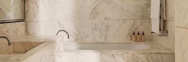 A sleek bathroom entirely clad in creamy-veined marble, with a built-in bathtub, modern sink, and polished chrome fixtures for a refined finish.