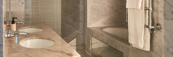 Elegant bathroom with dual marble sinks, chrome fixtures, a deep soaking tub with marble surround, and a heated towel rail with plush white towels.