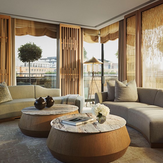 A sunlit corner of the Grand Pavilion living room featuring curved sofas, round marble coffee tables, and panoramic views framed by wood and glass elements.