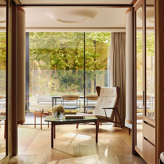 An elegant sitting area opening onto a private terrace, with floor-to-ceiling glass doors framing views of foliage and refined outdoor seating.