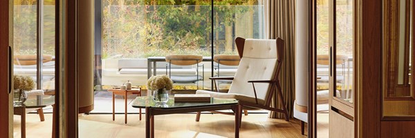An elegant sitting area opening onto a private terrace, with floor-to-ceiling glass doors framing views of foliage and refined outdoor seating.