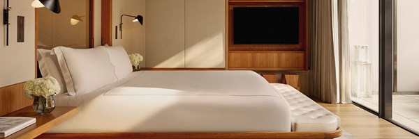 A peaceful bedroom featuring a sleek, low-profile bed dressed in white linens, with access to the private terrace through sliding glass doors.