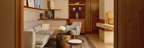 A refined sitting room with a button-tufted grey sofa, sculptural shelving showcasing curated objects, and soft lighting highlighting natural wood textures.