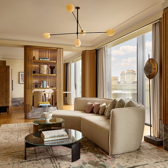 A stylish corner of the Hyde Park Penthouse living room, showcasing a curved sofa with plush cushions, floor-to-ceiling windows, and sculptural lighting above.