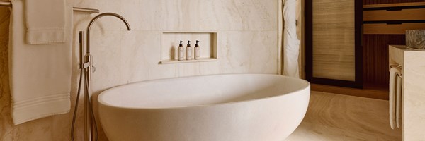 A luxurious marble-clad bathroom with a freestanding oval stone bath, soft lighting, and bespoke amenities neatly displayed in a recessed shelf.