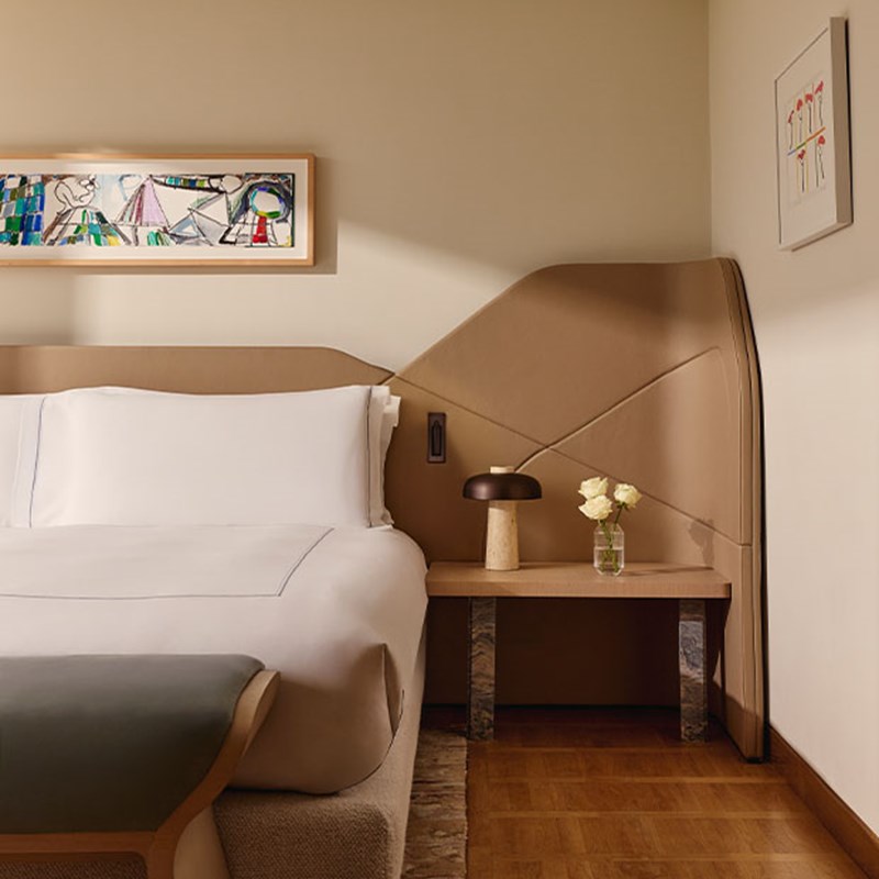 Contemporary bedroom with a sculptural leather headboard, crisp white linens, a minimalist bedside table with a petite lamp and fresh flowers, and vibrant modern artwork above the bed.