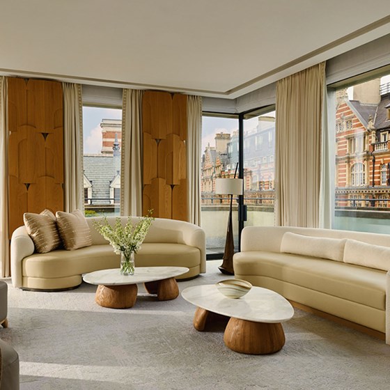 View of the contemporary penthouse living room showcasing curved sofas, textured armchairs, and elegant wood-paneled walls with panoramic city views.