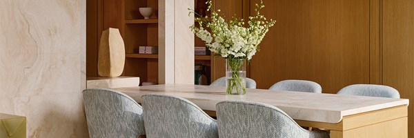 A close-up of the dining space with a sleek stone table, powder blue herringbone chairs, and a tall vase of white florals adding understated sophistication.