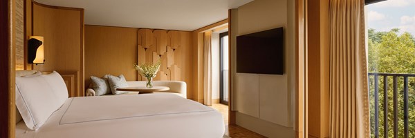 A luxurious bedroom view with plush bedding, a modern wall-mounted television, and a balcony door opening onto verdant treetop views.