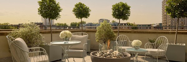 A sun-drenched private terrace adorned with elegant outdoor seating, manicured greenery, and a modern firepit, set against a panoramic London skyline.