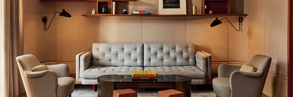 Sophisticated living room with a grey tufted sofa, two cream armchairs, a dark marble coffee table, and wall-mounted shelving with books and décor.