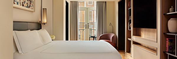 Bright bedroom with a large white bed, soft neutral walls, modern lighting, and balcony doors letting in natural light.