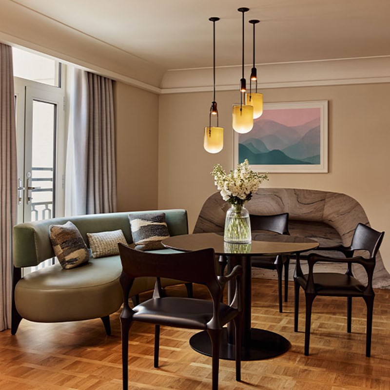 Contemporary dining area with a round table, black chairs, soft green bench seating, floral centerpiece, and hanging pendant lights.