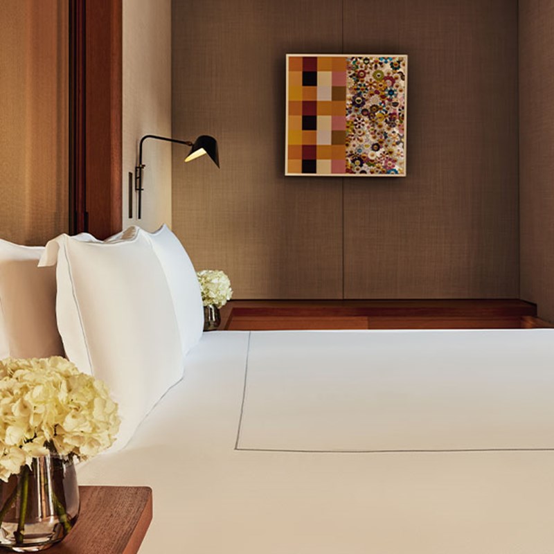 Close-up of a bed with crisp white linens, a bedside vase of hydrangeas, and a colorful abstract art piece above the headboard.