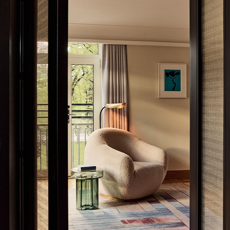 Cozy reading nook featuring a boucle-textured sculptural chair, a green glass side table with books, and a floor lamp near a window.