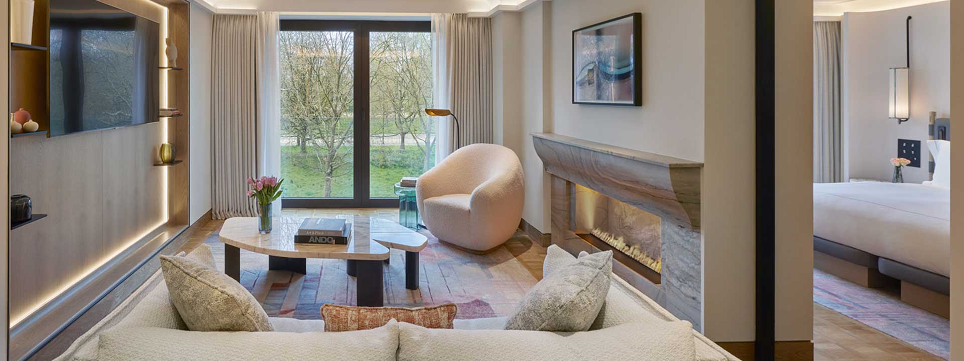 A separate lounge with a modern fireplace in the Park Suite, with a comfortable armchair and sofa in pastel colours.