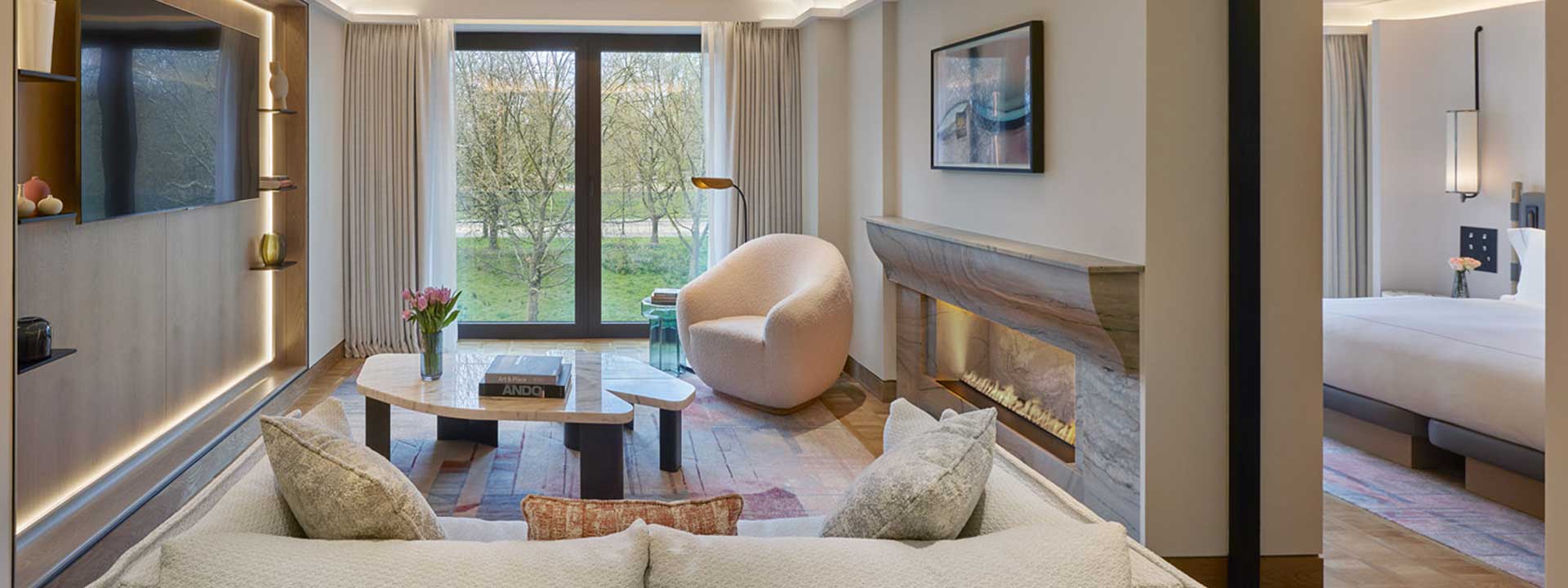 A separate lounge with a modern fireplace in the Park Suite, with a comfortable armchair and sofa in pastel colours.
