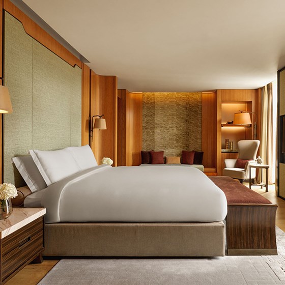 A beautifully composed bedroom featuring a crisp king-size bed, soft sage green wall panels, and rich wood detailing, accented by plush seating and ambient lighting.
