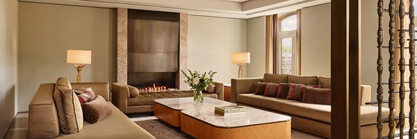 A refined sitting room with velvet sofas, a modern linear fireplace, and sculptural lighting, framed by tall windows and softened by neutral hues and tactile finishes.