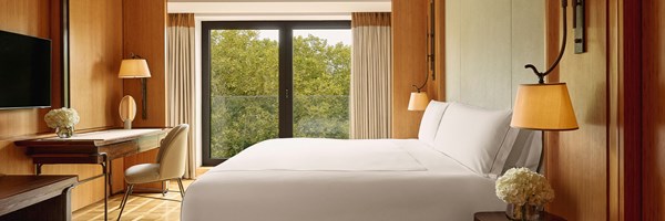 A peaceful guest bedroom with clean-lined design, elegant bedside lighting, and a balcony that opens to lush treetop views, complemented by a writing desk and soft furnishings.