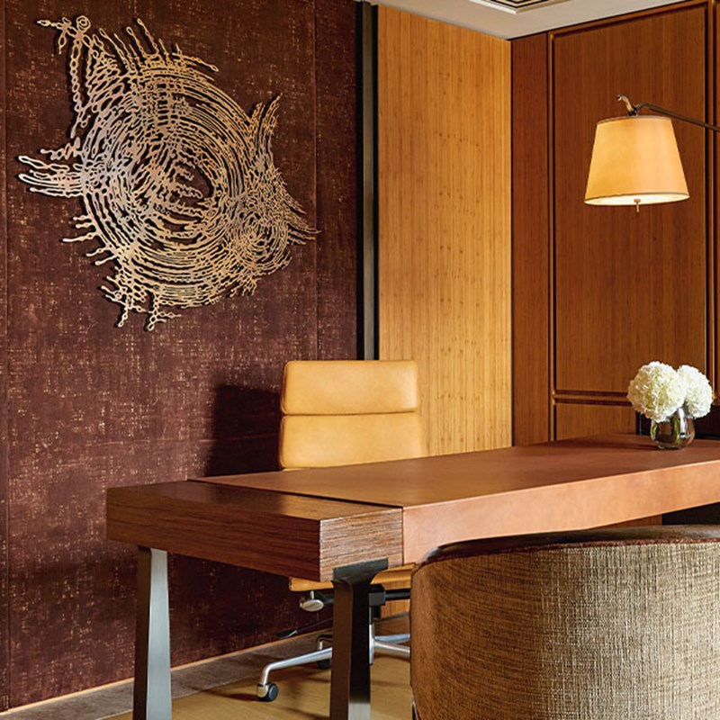 Sophisticated study space featuring a sleek wooden desk, caramel leather chair, ambient lighting, and a modern metallic wall sculpture on a rich textured backdrop.