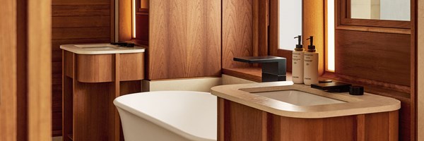 Modern bathroom with a white freestanding bathtub, dual stone-topped vanities, black fixtures, and warm wood cabinetry.