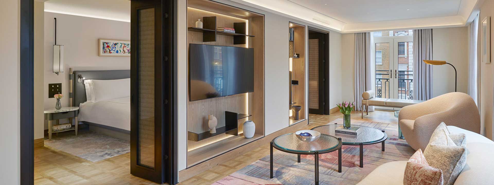 A view of the living room with TV and comfortable beige furniture in the Knightsbridge Suite, with lots of natural light.