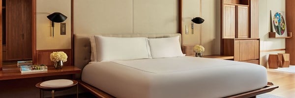 The bedroom of the Terrace Junior Suite at The Berkeley showing a modern wood-accented bed, fresh flowers, and art books on a built-in desk, with a large floral artwork on the wall.