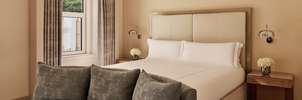 A bedroom in the Terrace Junior Suite at The Berkeley with a king-sized bed, taupe headboard, and bedside tables with chrome sconces and fresh white flowers.