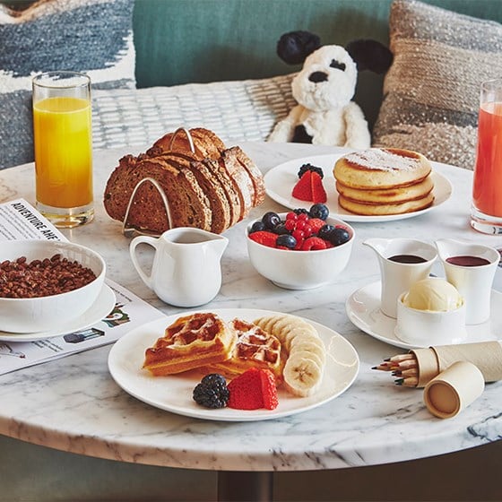 Children's breakfast in suite featuring coco pops, orange juice, toast, berries, pancakes,colouring pencils and jellycat toy dog
