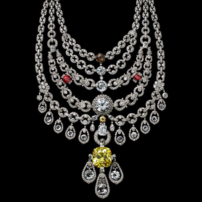 Cartier high jewellery necklace featuring five diamond-studded chains, red and brown gemstones, and a large yellow diamond pendant, displayed against a black background.