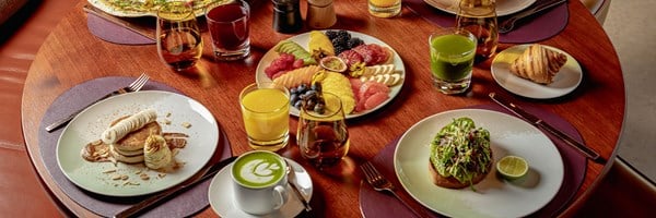 Colourful breakfast spread at The Berkeley with pancakes, avocado toast, fresh fruit, juices, croissant, and matcha latte, arranged on a round wooden table.