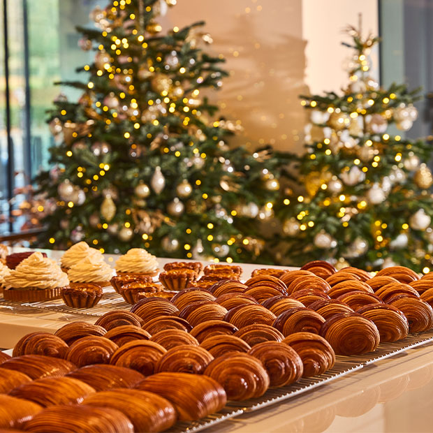 Festive pastry display of croissants and desserts set in front of decorated Christmas trees.