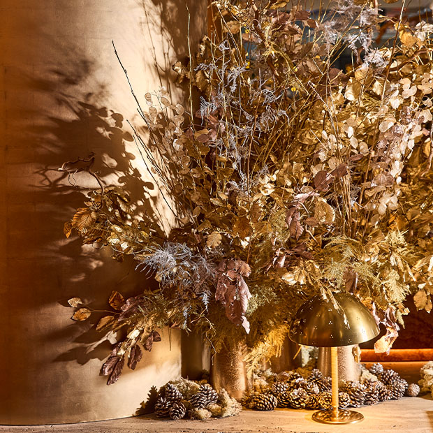 Seasonal dried floral arrangement with gold leaves, pinecones, and soft ambient lighting.