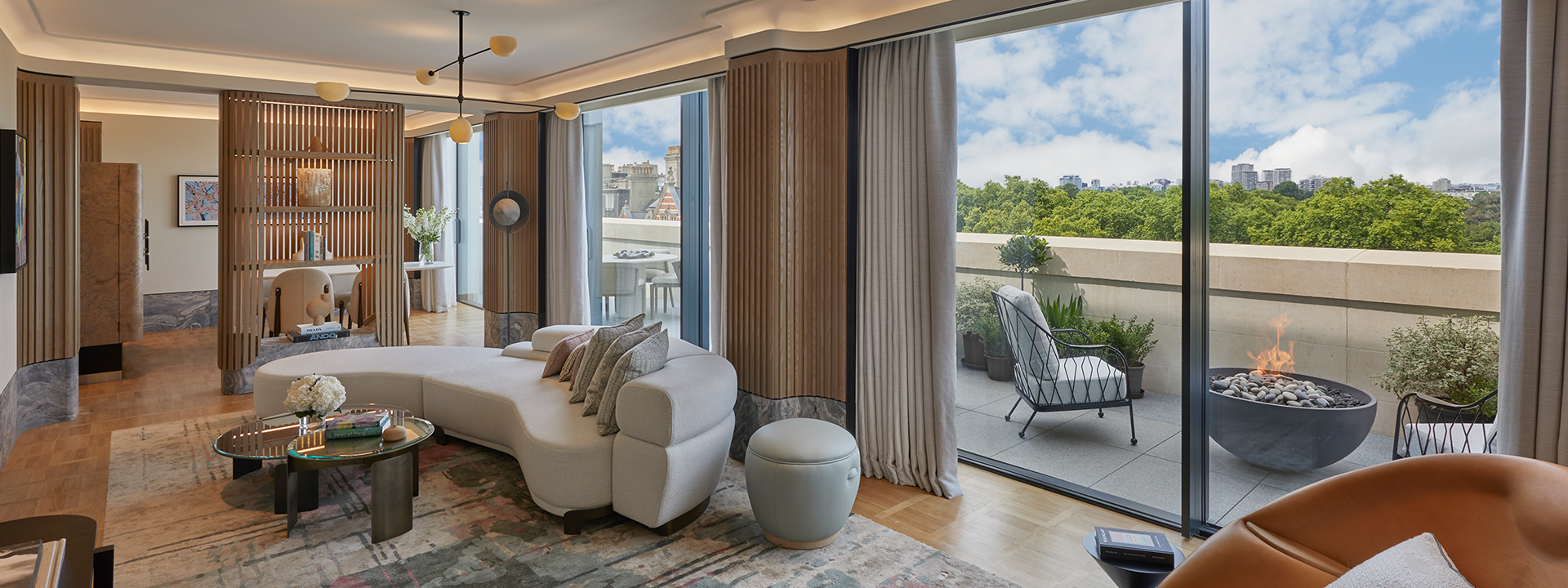 A lounge in a suite with a curved sofa and coffee table, and a terrace with a view on Hyde Park