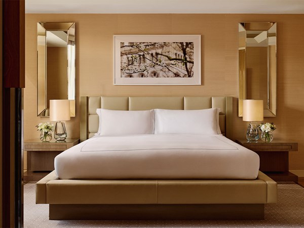 Modern bedroom with king bed, padded headboard, symmetrical mirrors, and warm beige tones.