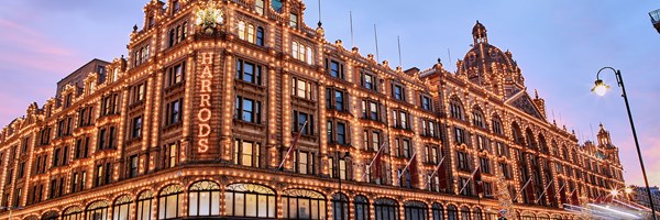 Harrods’ exterior at dusk, its historic façade outlined in warm festive lights under a pink-blue sky.