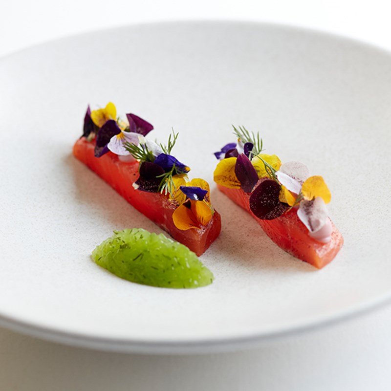 Two slices of raw salmon with edible flowers on top.