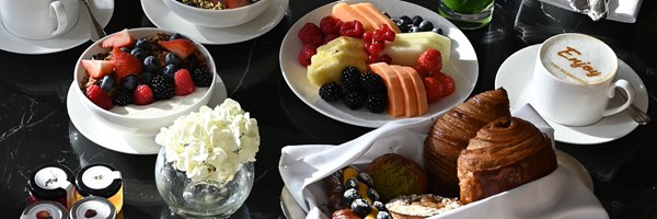 a selection of breakfast including pastries, fruit and yogurt, with a vase of white flowers